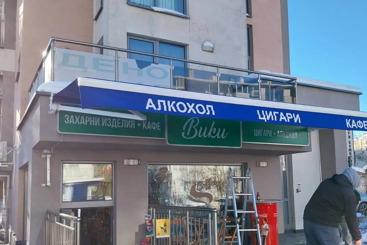 Брандирана прибираща се тента със син и зелен плат над вход на магазин